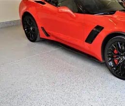 Red sports car parked on a gray full flake garage floor coating.